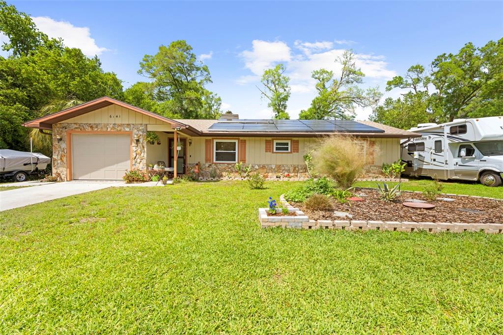 A single-story house with stone accents, solar panels, a garage, and an RV parked alongside — 6141 E DELL LANE, INVERNESS, FL