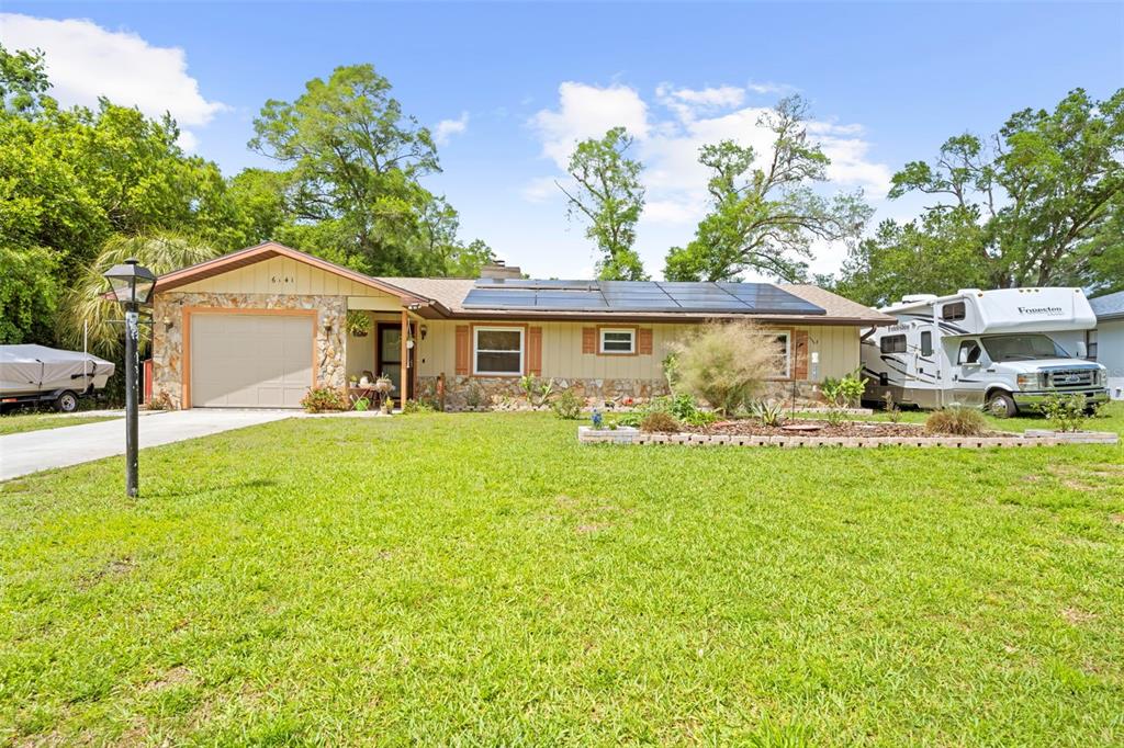 A single-story house with a stone-accented garage, solar panels, and an RV parked alongside — 6141 E DELL LANE, INVERNESS, FL