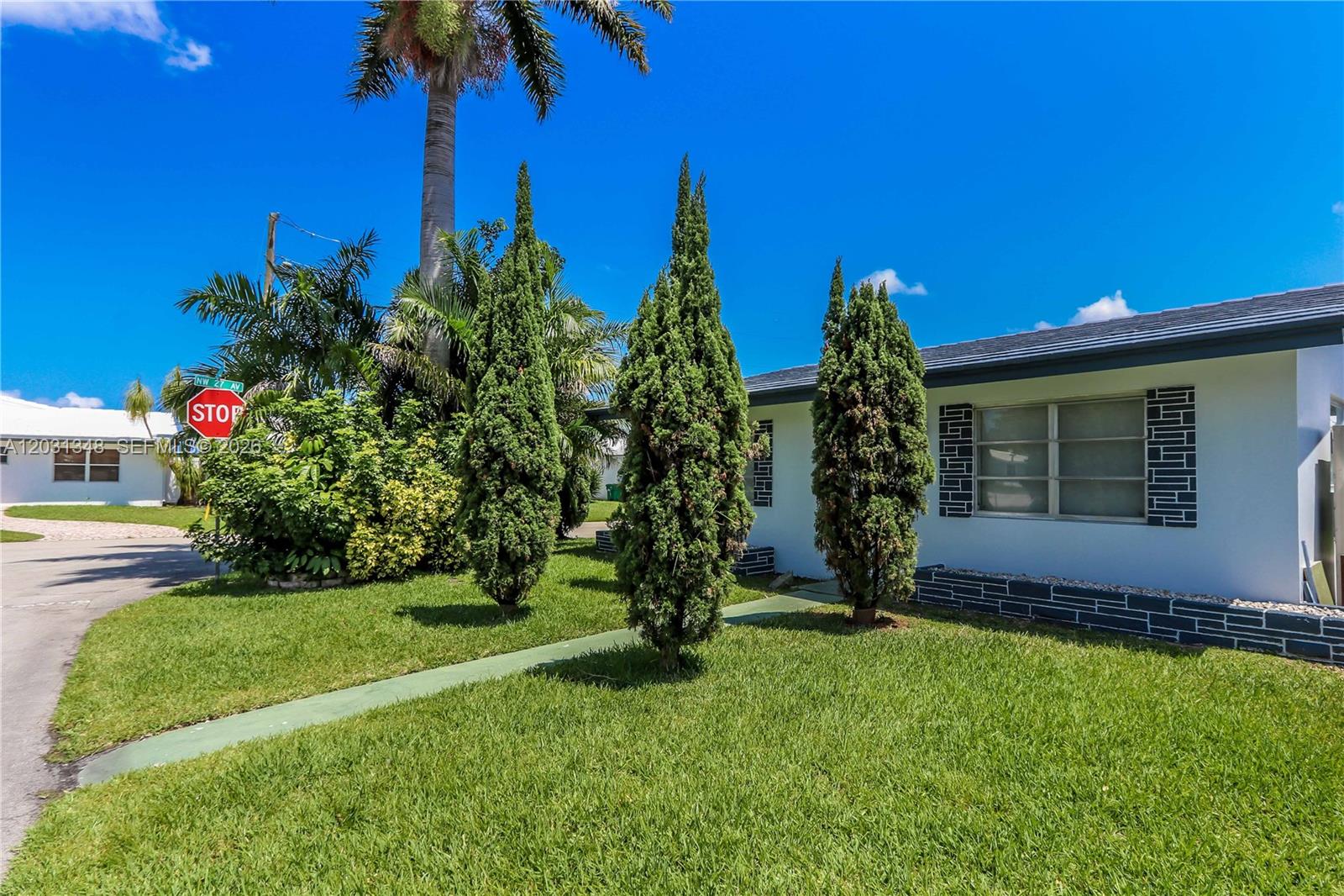 A white house exterior features a green lawn, three tall evergreen trees, and a stop sign — 2700 NW 52nd Ct, Tamarac FL 33309, TAMARAC, FL