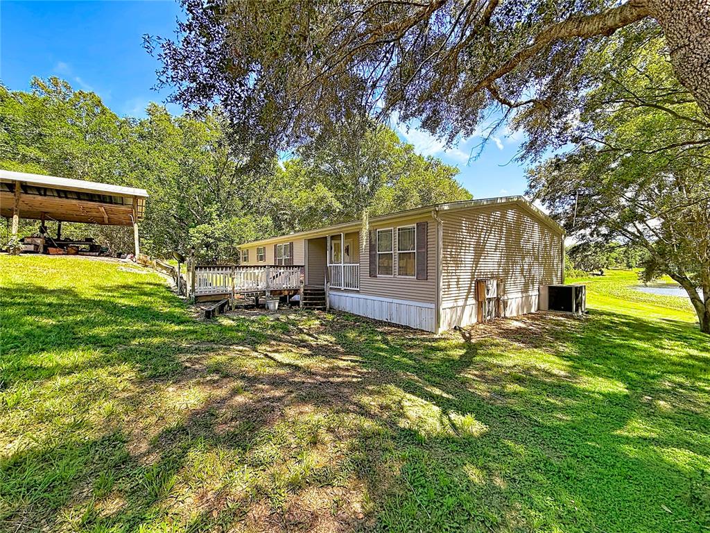 A tan manufactured home with a wooden deck sits on a grassy lot with trees — 29714 SE HIGHWAY 42, UMATILLA, FL