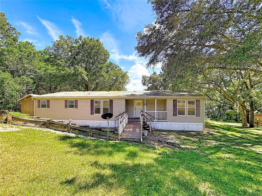 A single-story manufactured home with tan siding, a wooden ramp, and surrounding trees — 29714 SE HIGHWAY 42, UMATILLA, FL