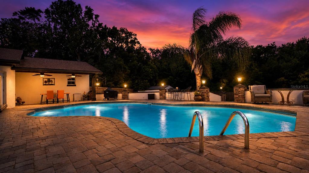 A backyard swimming pool with a stone patio and covered patio area at sunset — 122 BEARSS CIRCLE, LONGWOOD, FL