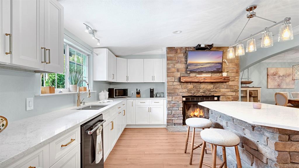 A kitchen features white cabinets, stone fireplace, and a breakfast bar with two stools — 122 BEARSS CIRCLE, LONGWOOD, FL