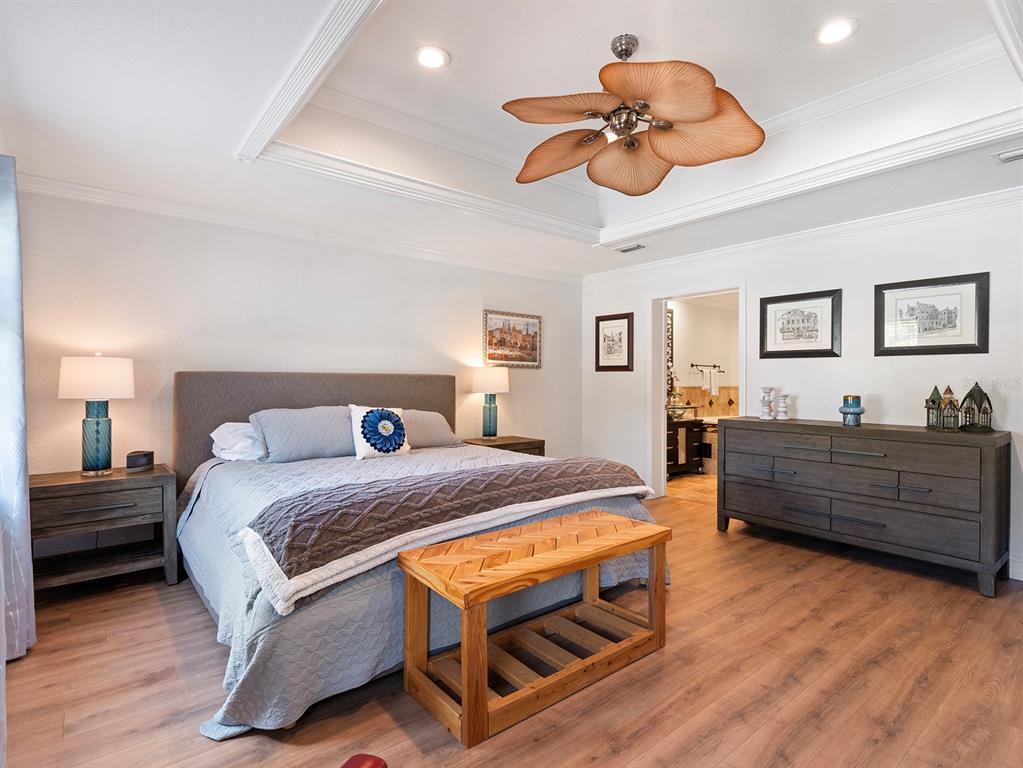 A bedroom features a tray ceiling with a palm-leaf fan, wood flooring, and gray furniture — 122 BEARSS CIRCLE, LONGWOOD, FL