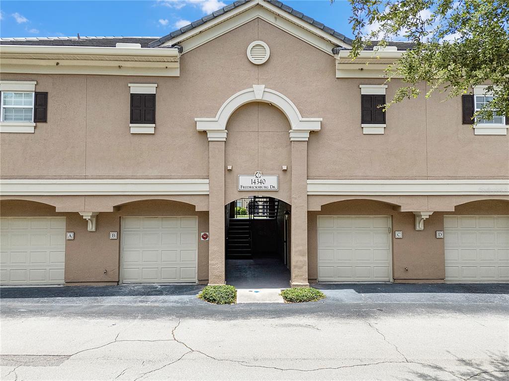 The exterior of a two-story building features four garage doors and a central stairwell entrance — 14340 FREDRICKSBURG DRIVE UNIT 701, ORLANDO, FL