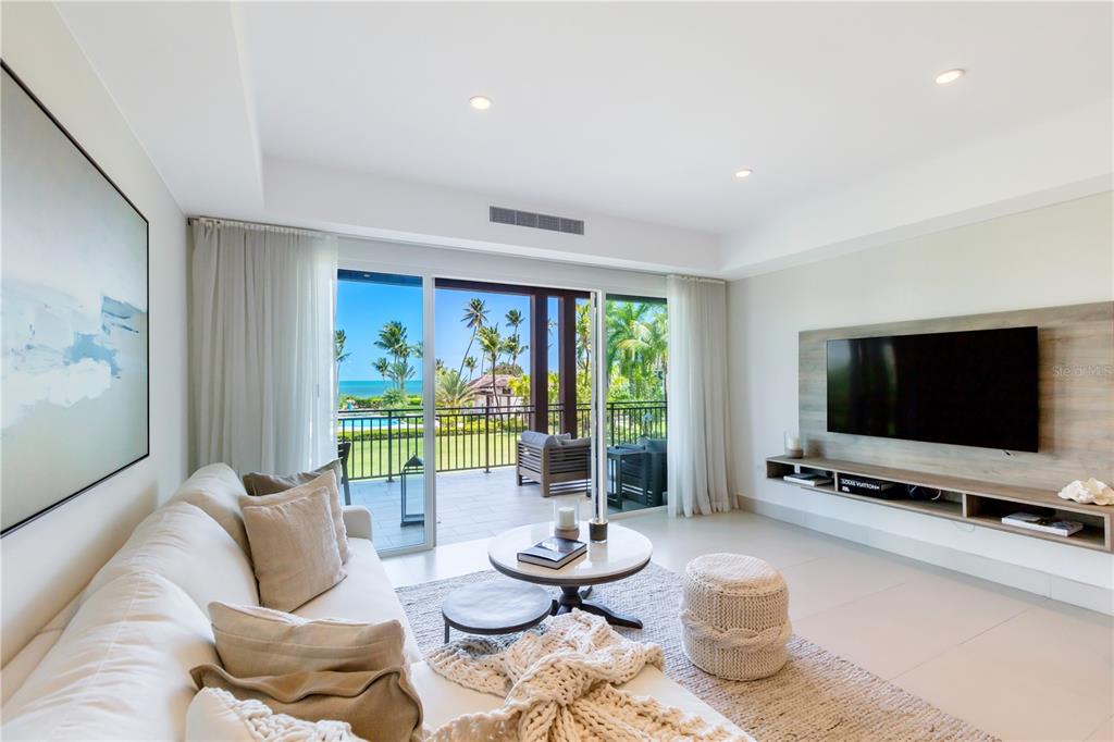 A modern living room features a white sofa, a television, and a balcony overlooking the ocean — Bahia Beach Golf Club LAS VENTANAS II UNIT 208, RIO GRANDE, PR