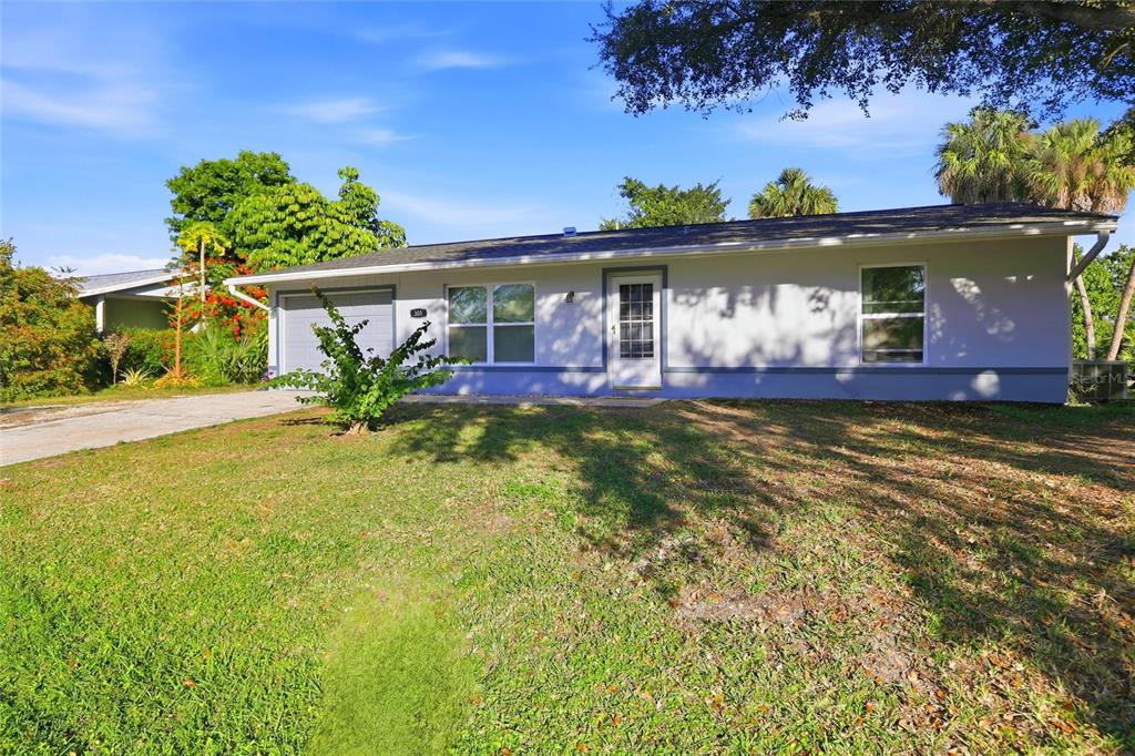 A single-story house with a light-colored exterior, a front-facing garage, and a large grassy yard — 301 LAMBERT STREET, PORT CHARLOTTE, FL