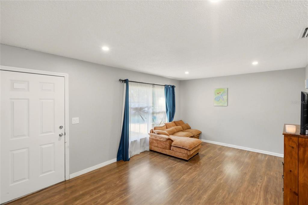 A living room with light gray walls, wood-look flooring, a brown sectional, and blue curtains — 301 LAMBERT STREET, PORT CHARLOTTE, FL