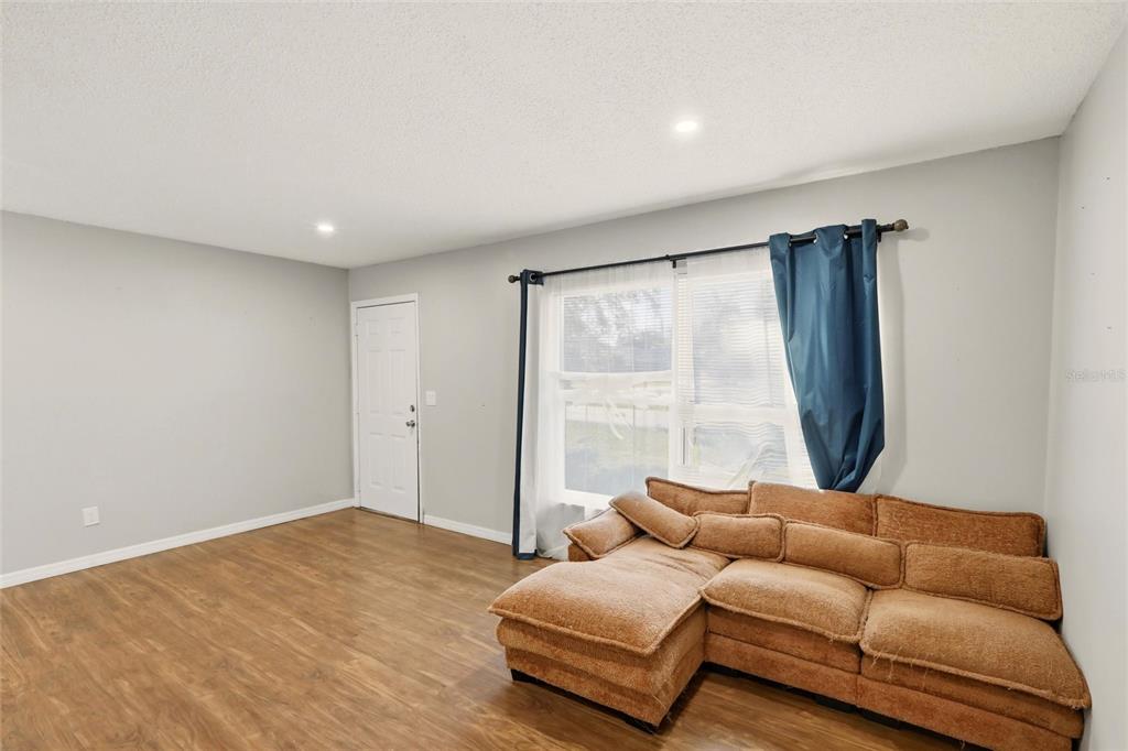 A living room features light gray walls, wood-look flooring, a large window, and a brown sectional — 301 LAMBERT STREET, PORT CHARLOTTE, FL