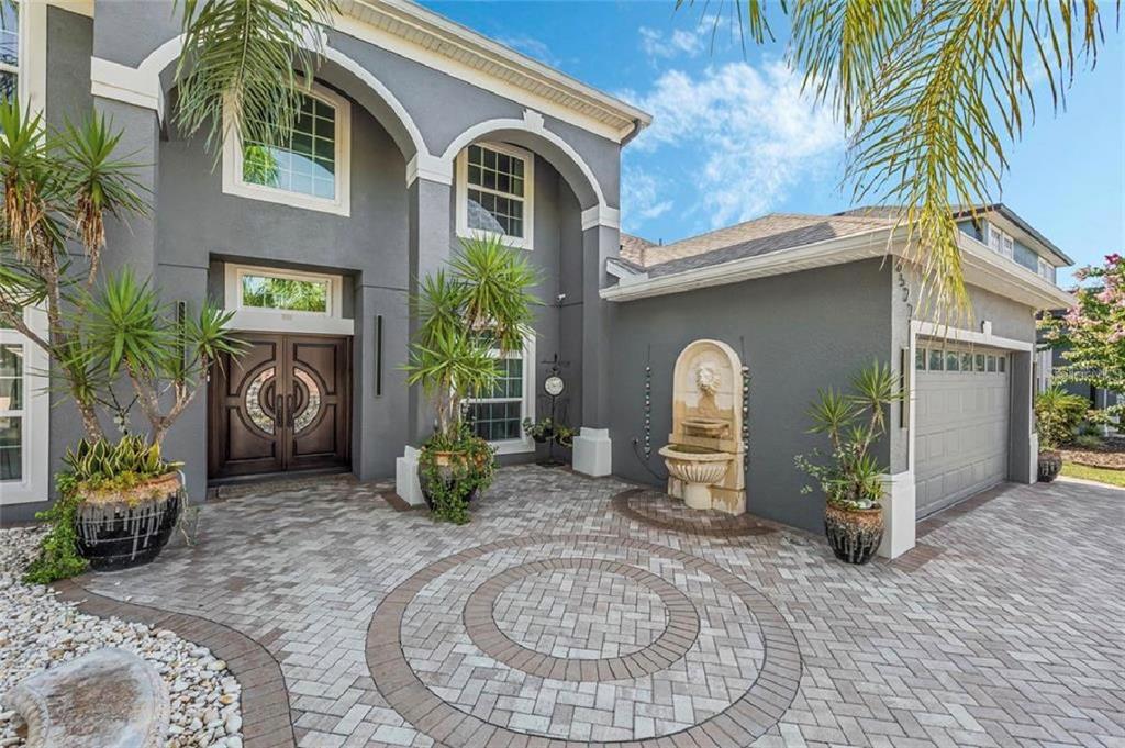 A gray two-story house features a paved circular driveway, a stone fountain, and double doors — 6527 BAYBORO COURT, ORLANDO, FL