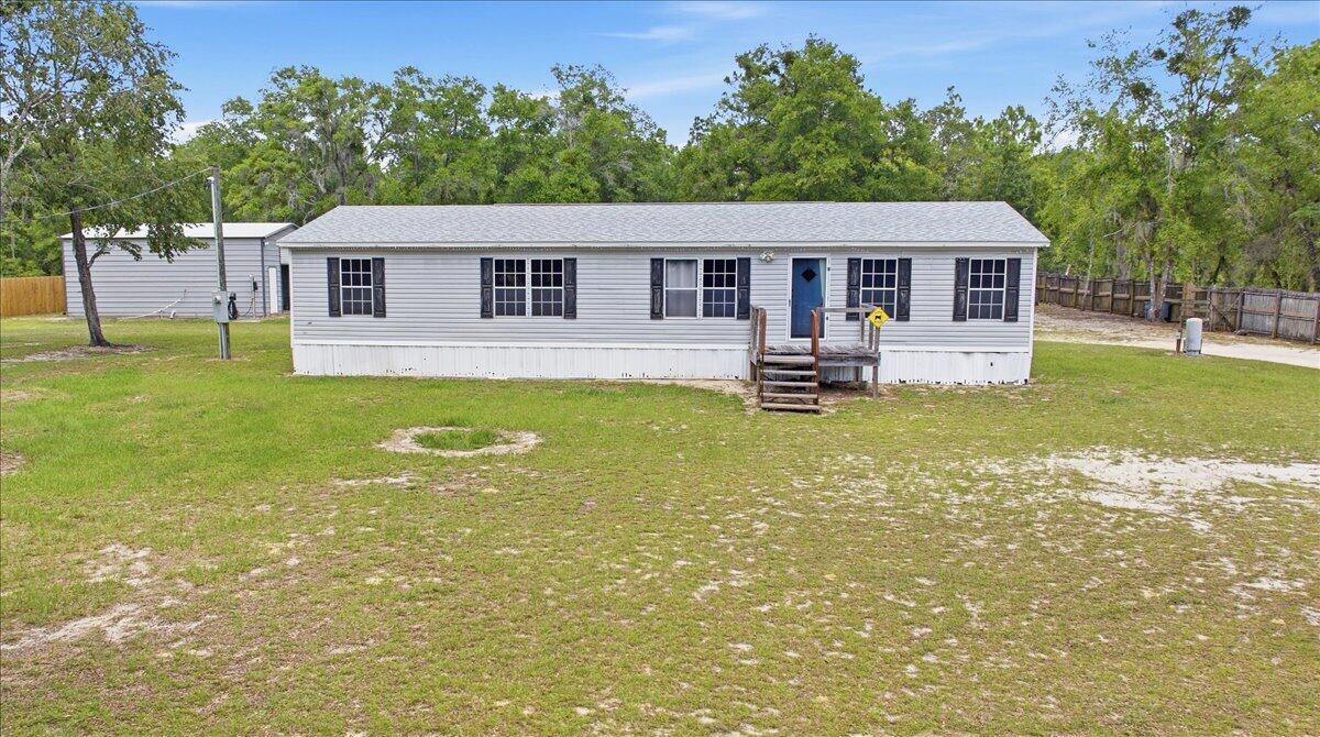 A single-story manufactured home with gray siding sits on a grassy lot with trees — 194 Keuka Road, FL 32148, FL