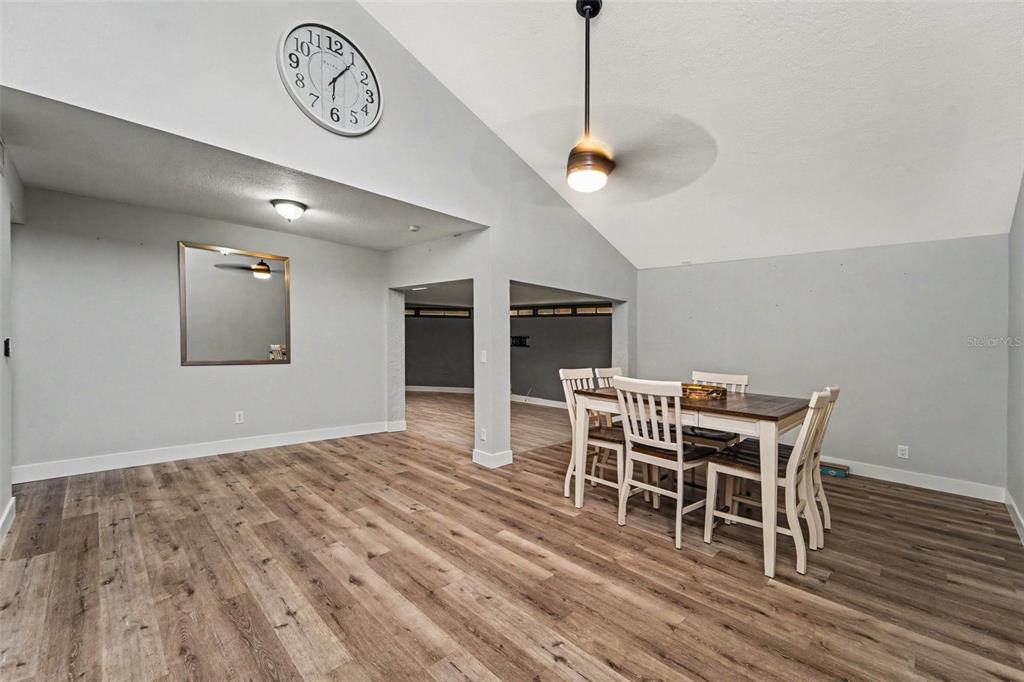 A dining area with wood-look flooring, a vaulted ceiling, a ceiling fan, and a wall clock — 2737 HAVERHILL COURT, CLEARWATER, FL