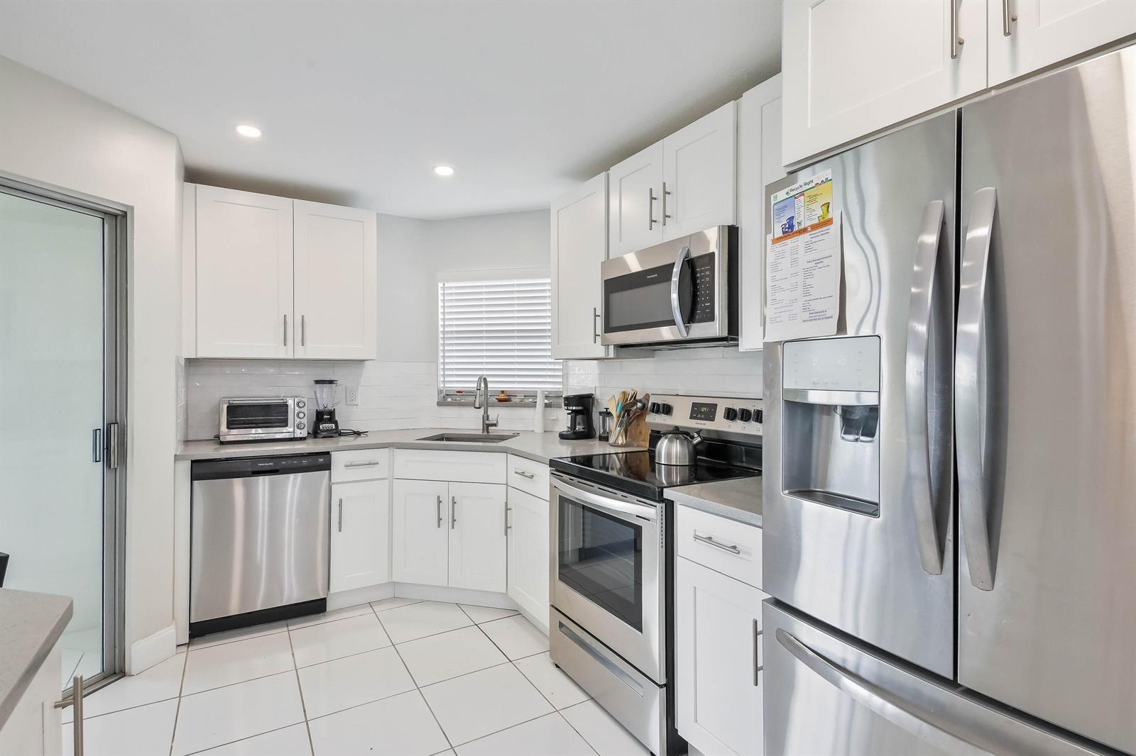 A kitchen features white cabinets, stainless steel appliances, a corner sink, and white tile flooring — 3661 Via Poinciana # 616, FL 33467, FL