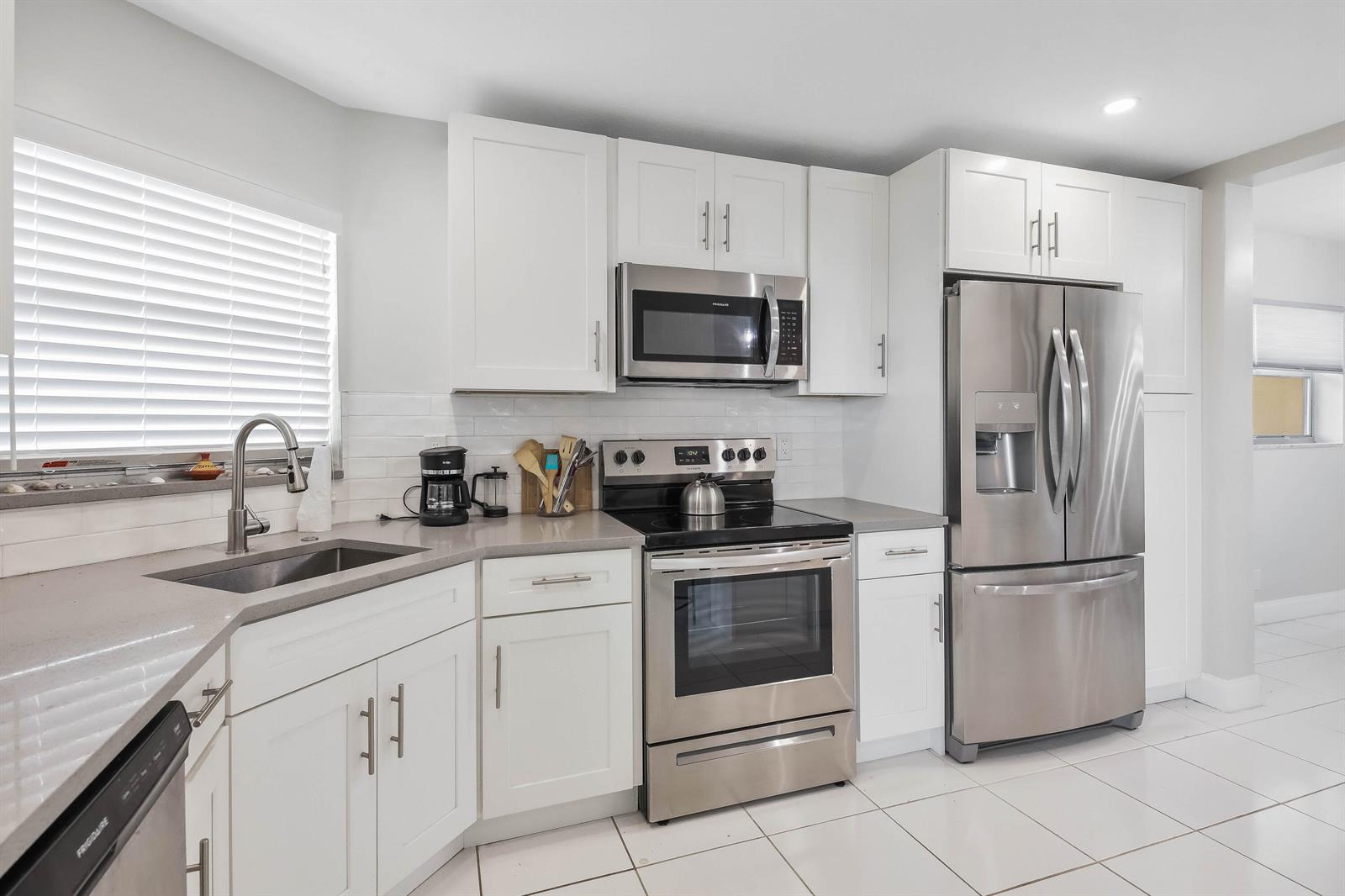A modern kitchen features white cabinets, stainless steel appliances, and gray countertops — 3661 Via Poinciana # 616, FL 33467, FL