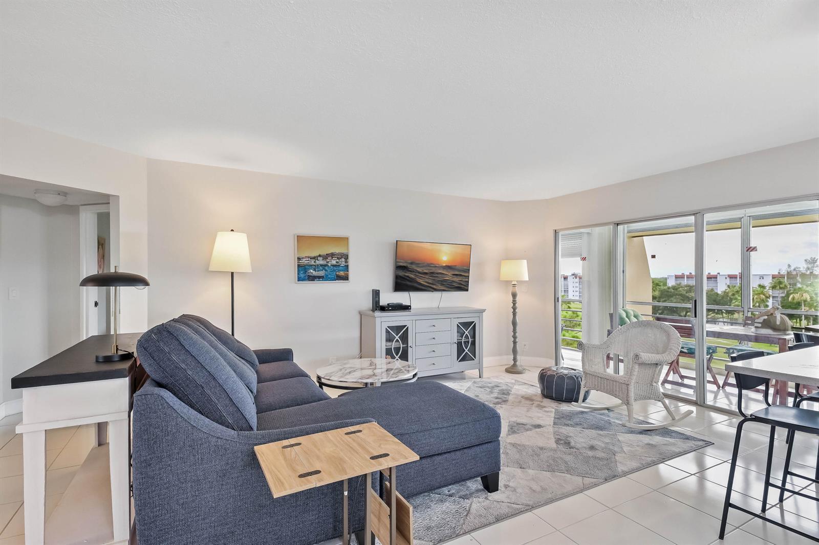 A living room features a blue sectional sofa, a television, and a sliding glass door — 3661 Via Poinciana # 616, FL 33467, FL
