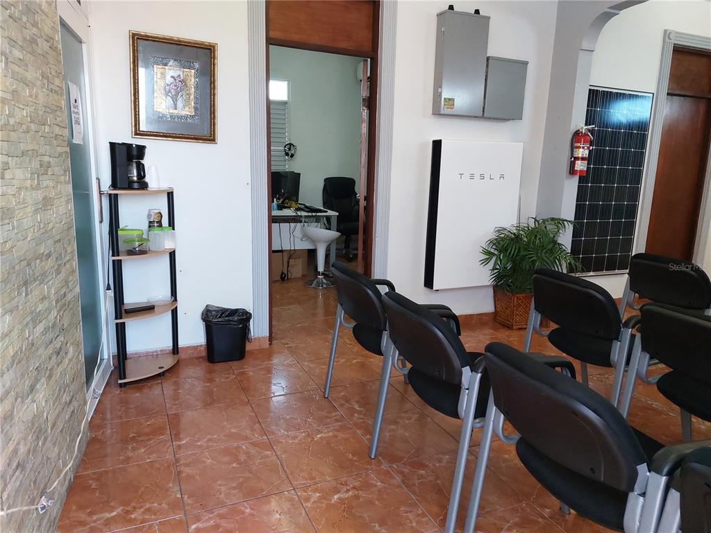 A waiting area features tile floors, several black chairs, and a wall-mounted Tesla Powerwall unit — Calle Villa ESQUINA CALLE PROGRESO, PONCE, PR