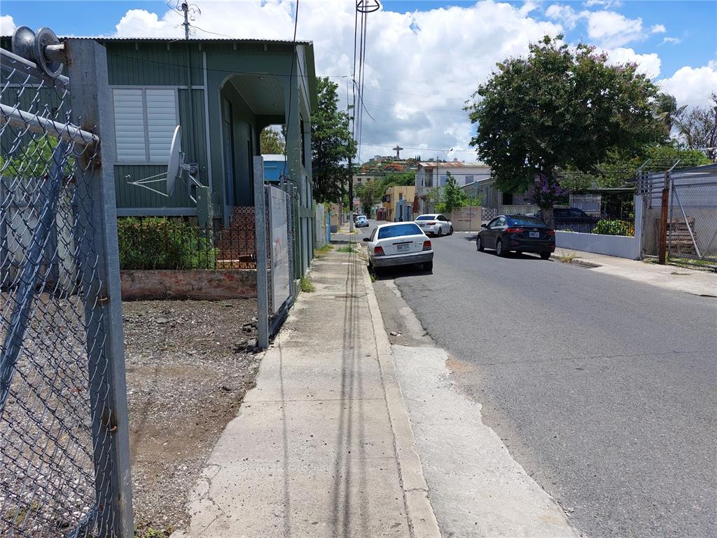 A street view shows a sidewalk, a green wooden house, and parked cars under a sky — Calle Villa ESQUINA CALLE PROGRESO, PONCE, PR