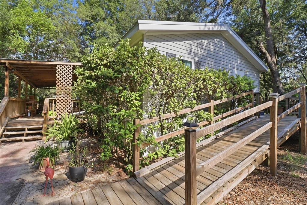 A wooden wheelchair ramp leads to the side entrance of a light-colored mobile home — 6845 W JACKSON LANE, HOMOSASSA, FL