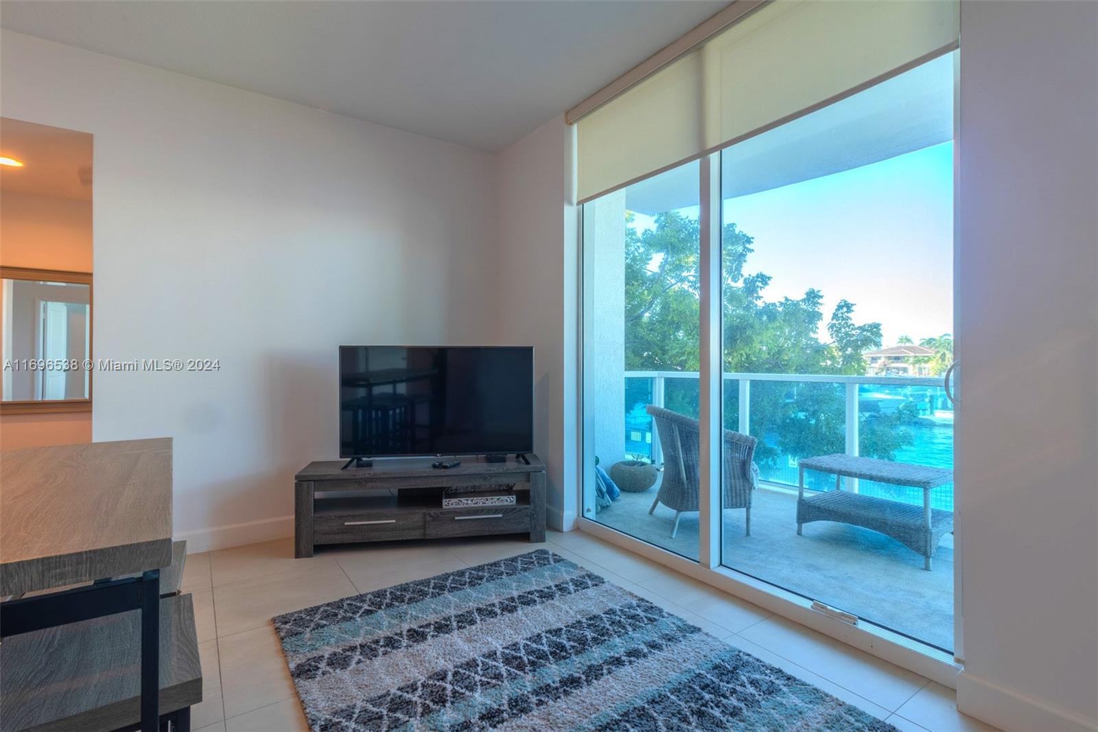 A living room features a television on a wooden stand, a patterned rug, and a balcony — 1945 S Ocean Dr # M5, Hallandale Beach FL 33009, HALLANDALE BEACH, FL