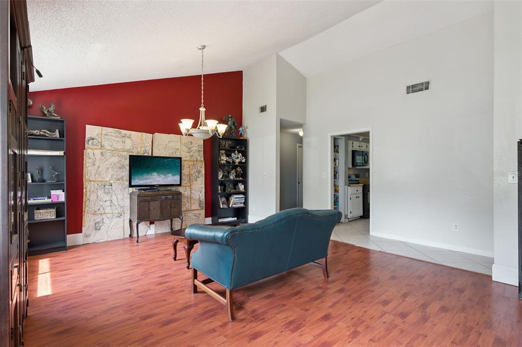 A living room features wood-look flooring, a red accent wall, and a blue leather sofa — 971 WAVERLY DRIVE, LONGWOOD, FL
