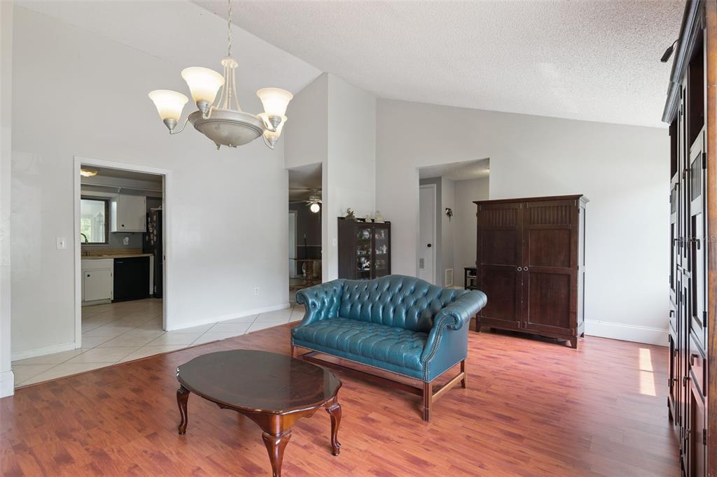 A living room with wood-look flooring, a teal tufted sofa, and a dark wood armoire — 971 WAVERLY DRIVE, LONGWOOD, FL