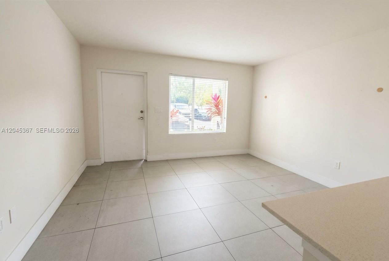 An empty room features light-colored tile flooring, white walls, a window, and a door — 2535 NE 193rd St # 3104, Miami FL 33180, MIAMI, FL