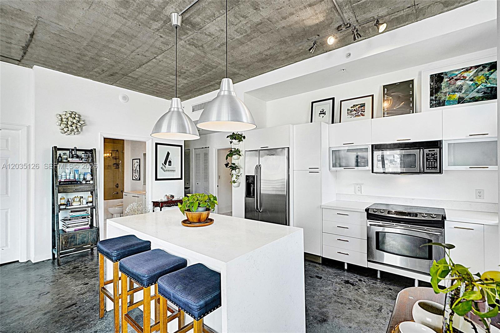 A modern kitchen features a white island, stainless steel appliances, and an exposed concrete ceiling — 133 NE 2nd Ave # 1013, Miami FL 33132, MIAMI, FL