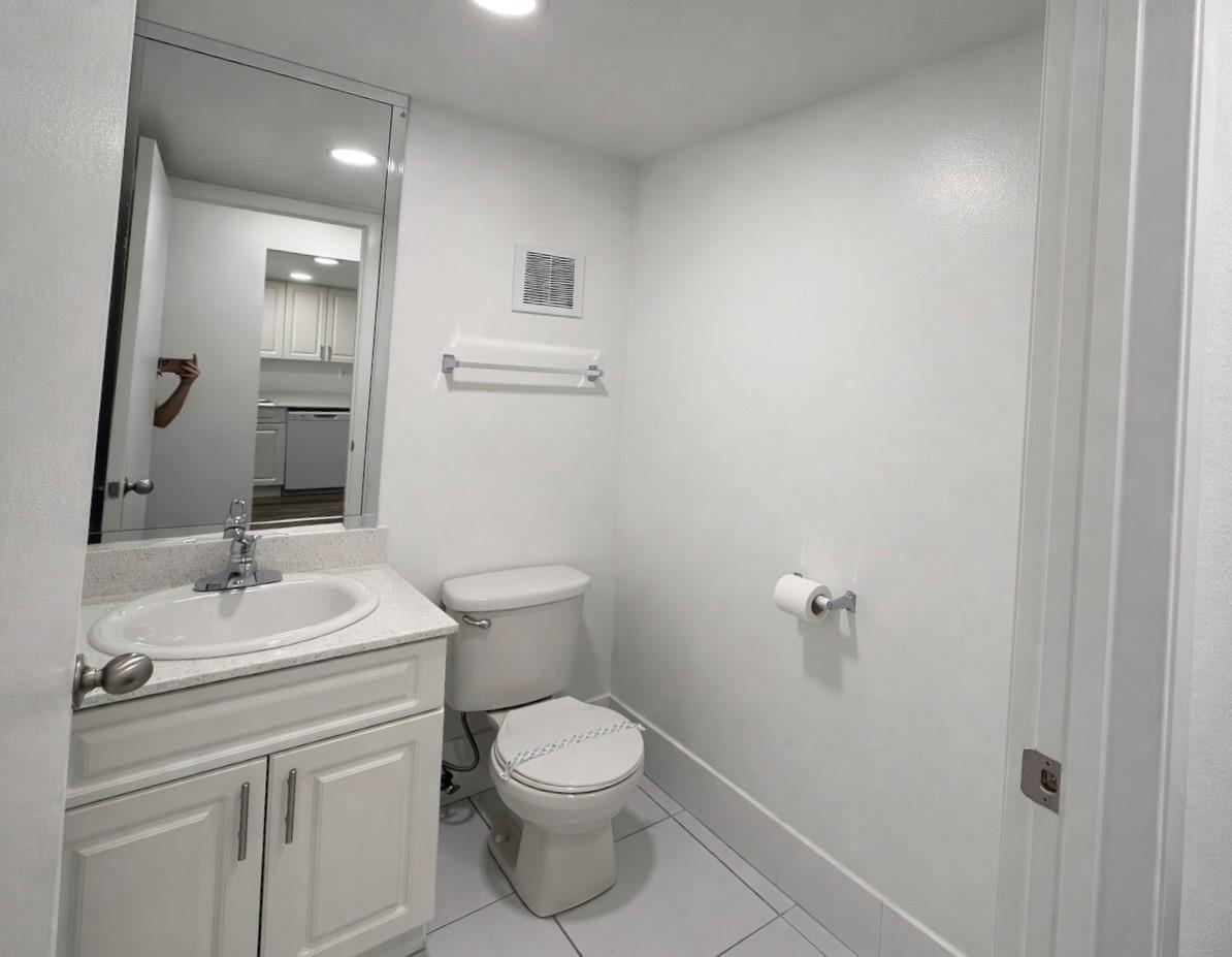 A small bathroom with a white vanity, toilet, and a large mirror on a white wall — 17350 NW 68th Avenue # 404, Hialeah FL 33015, HIALEAH, FL