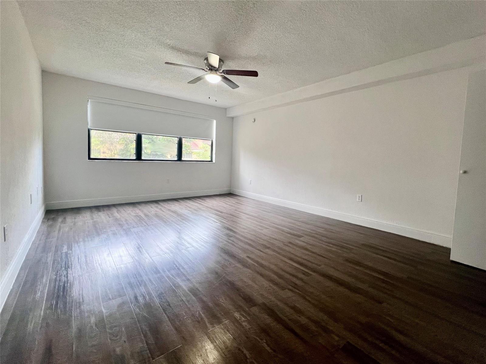 An empty room features white walls, dark wood-look flooring, and a ceiling fan — 17350 NW 68th Avenue # 404, Hialeah FL 33015, HIALEAH, FL
