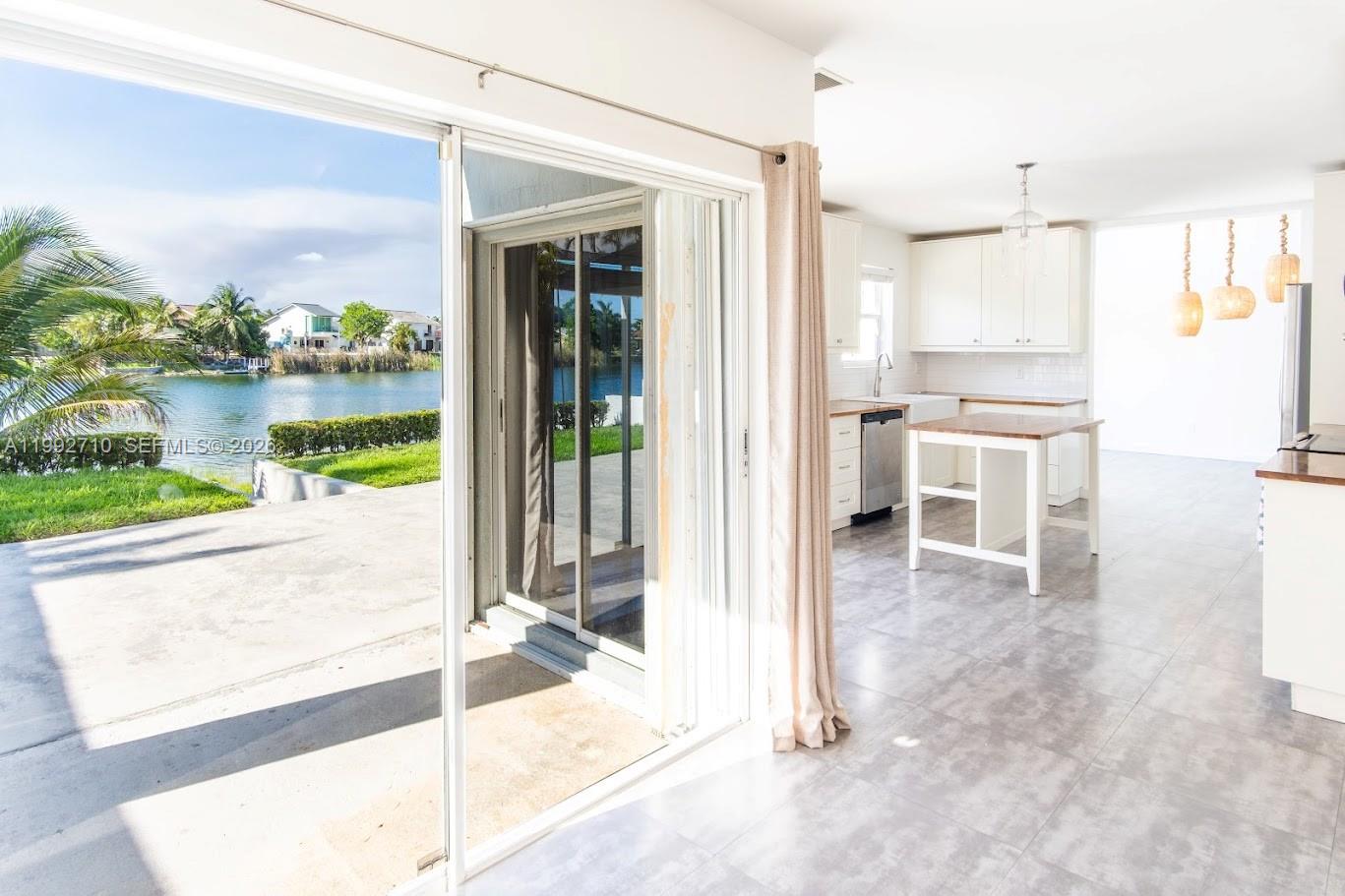 A kitchen with white cabinets and a wooden island opens to a patio overlooking water — 15511 SW 59th St, Miami FL 33193, MIAMI, FL