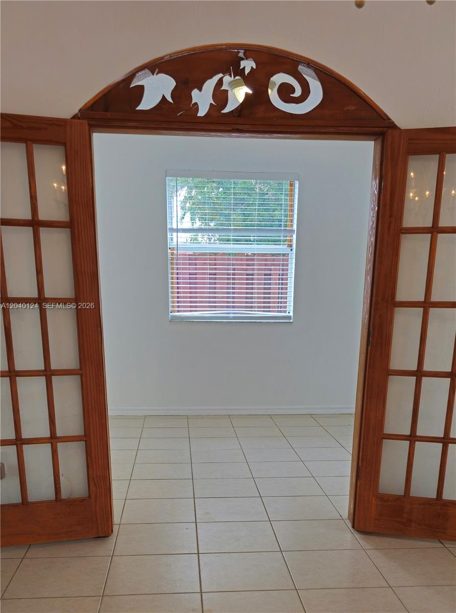 A room with tile flooring is viewed through open wooden French doors with decorative trim — 2410 SW 153rd Pass, Miami FL 33185, MIAMI, FL