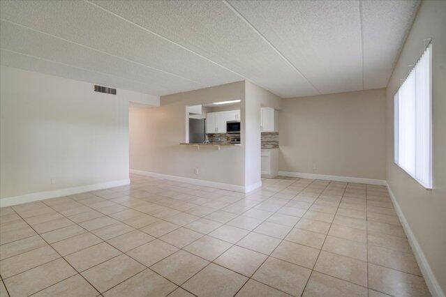 An empty living room with beige tile flooring and a pass-through window to the kitchen — 1104 Meadows Circle, Boynton Beach FL 33436, BOYNTON BEACH, FL