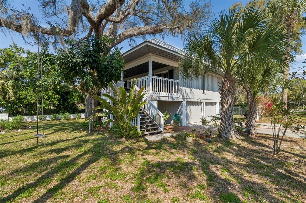 An elevated house with a white porch, stairs, and a large tree in the yard — 600 N MAYO STREET, CRYSTAL BEACH, FL