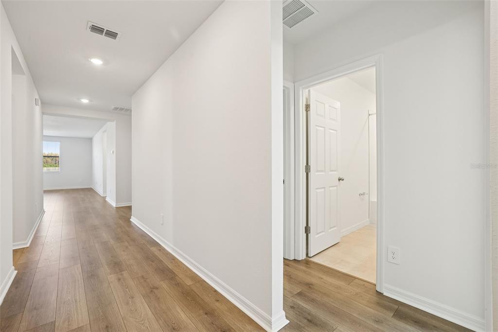 A hallway with wood-look flooring leads to a room with a window and a bathroom — 4505 EAGLE PERCH COURT, ST CLOUD, FL