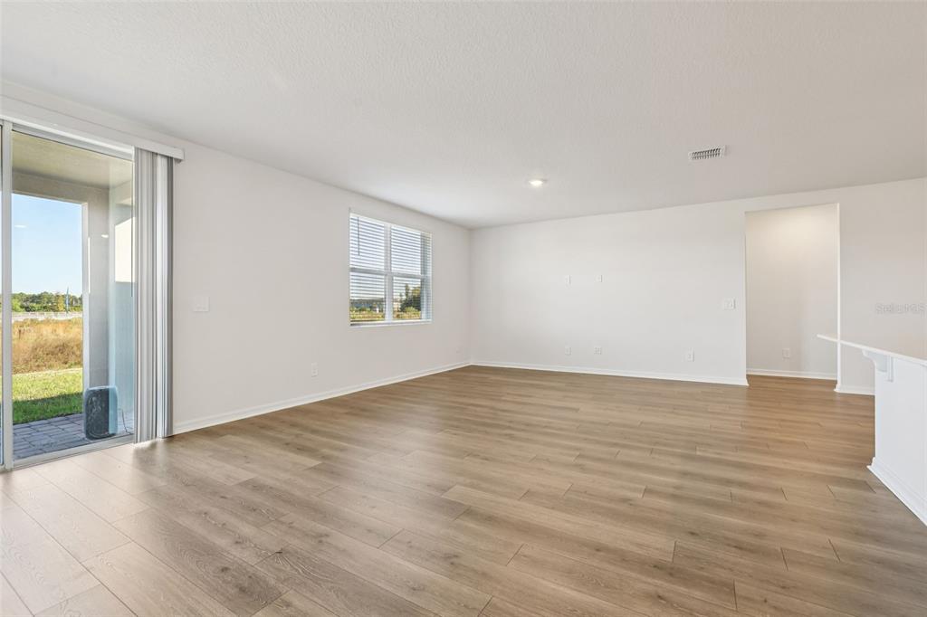 An empty living room with light wood-look flooring, white walls, and a sliding glass door — 4505 EAGLE PERCH COURT, ST CLOUD, FL