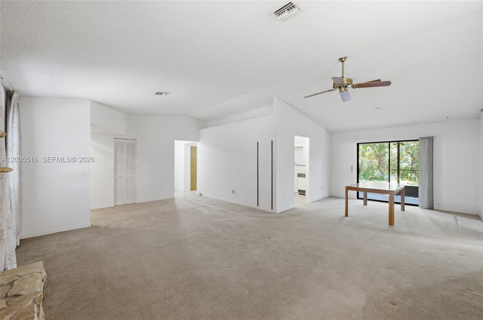 A spacious, carpeted living area features a vaulted ceiling, ceiling fan, and sliding glass doors — 642 Nobles St, Sebastian FL 32958, SEBASTIAN, FL