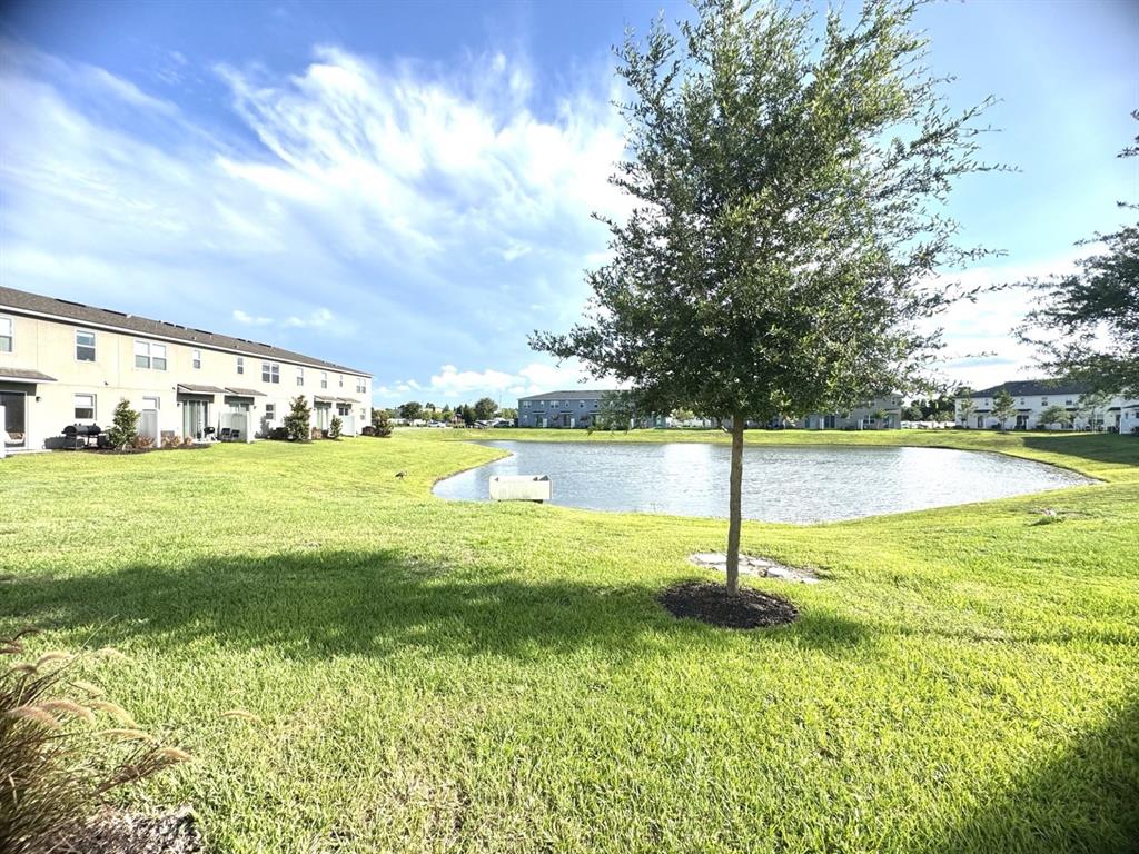 A grassy lawn leads to a small pond surrounded by multi-story residential buildings — 1025 SPRING PALMS LOOP, ORLANDO, FL