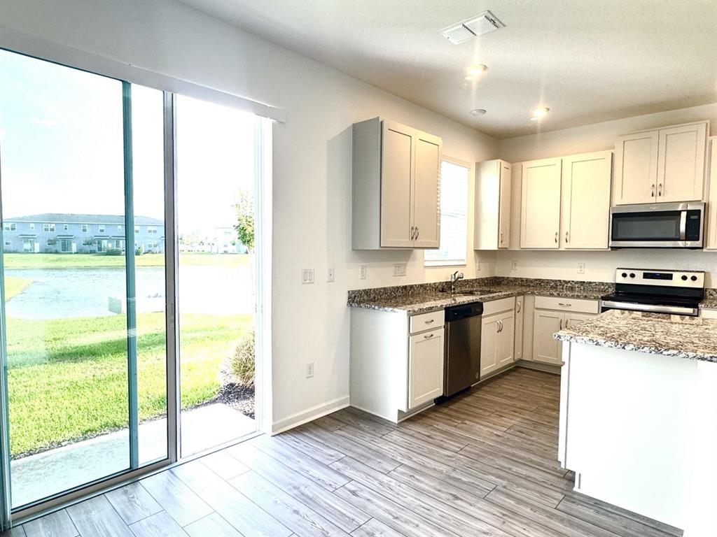 A kitchen with white cabinets, granite countertops, stainless steel appliances, and a sliding glass door — 1025 SPRING PALMS LOOP, ORLANDO, FL