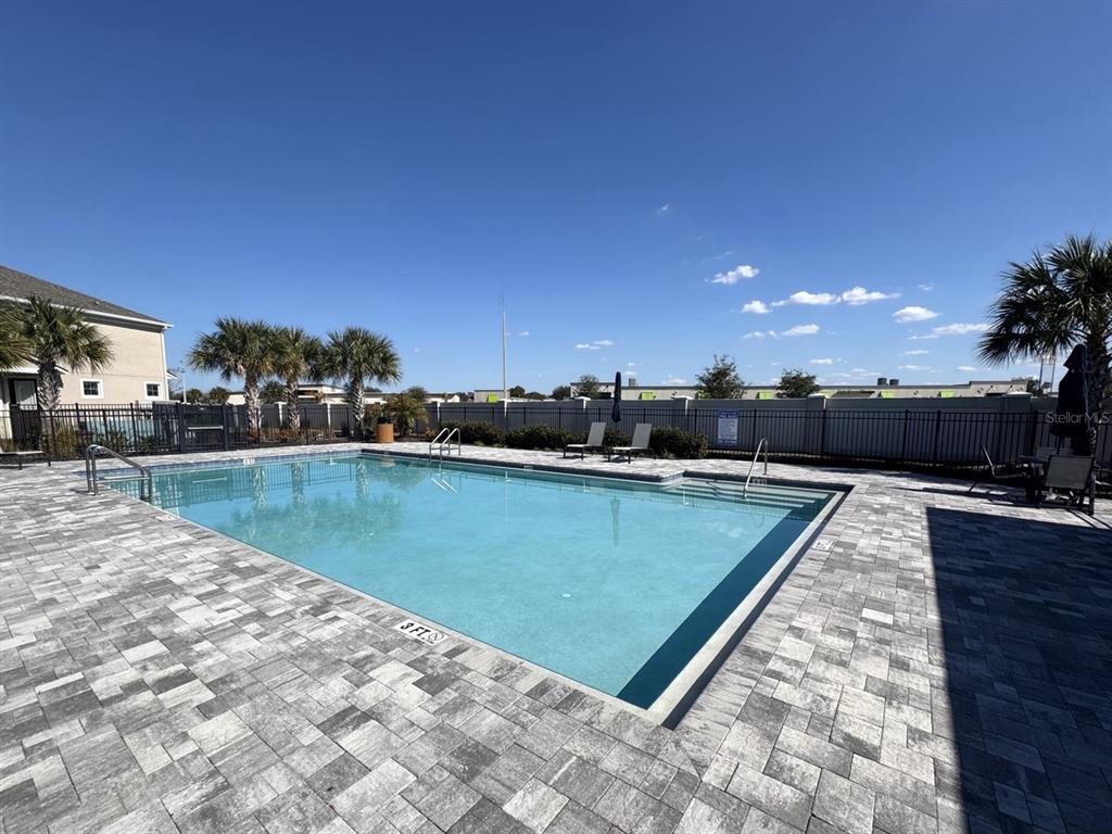 A rectangular swimming pool with a paved deck is surrounded by a black metal fence — 1025 SPRING PALMS LOOP, ORLANDO, FL