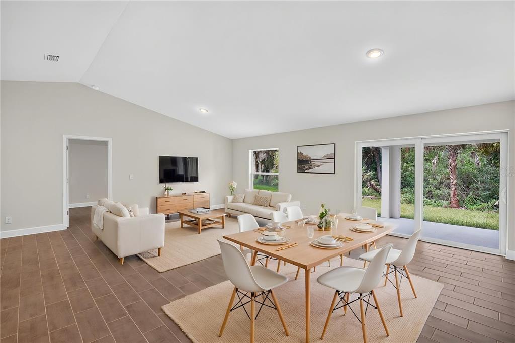A bright, open-concept living and dining area features tile flooring, vaulted ceilings, and sliding glass doors — 23175 WILKINSON AVENUE, PORT CHARLOTTE, FL