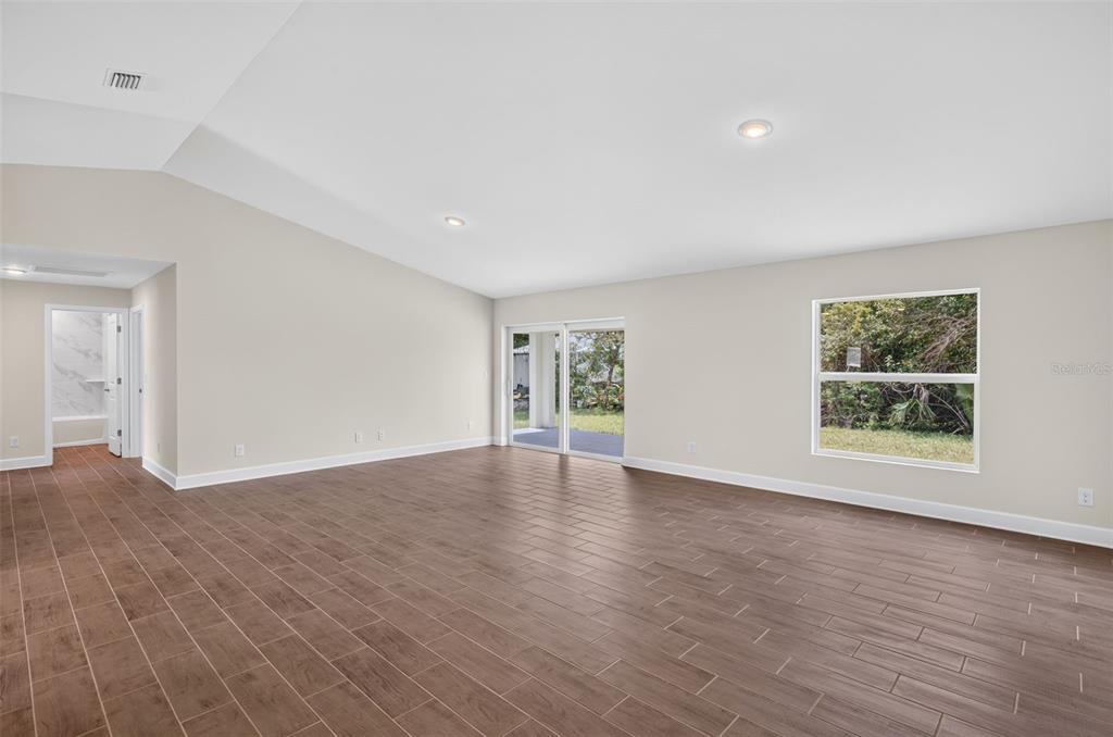 A spacious living room features wood-look tile flooring, recessed lighting, and sliding glass patio doors — 23175 WILKINSON AVENUE, PORT CHARLOTTE, FL