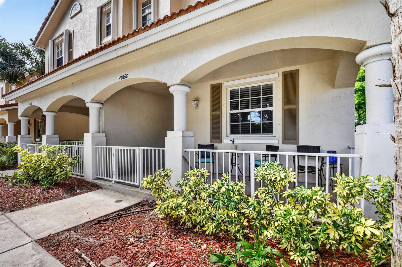 A covered patio with a white railing and chairs sits in front of a building — 4816 W Bexley Park Drive # C, Delray Beach FL 33445, DELRAY BEACH, FL