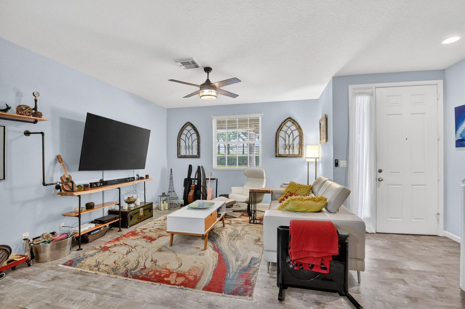 A living room features light blue walls, a patterned area rug, and a wall-mounted television — 4816 W Bexley Park Drive # C, Delray Beach FL 33445, DELRAY BEACH, FL
