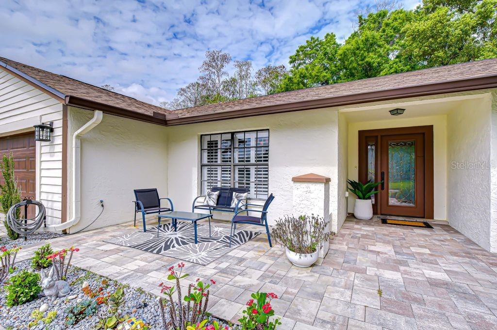 A paved patio area sits in front of a house with a brown front door — 16704 VALLELY DRIVE, TAMPA, FL