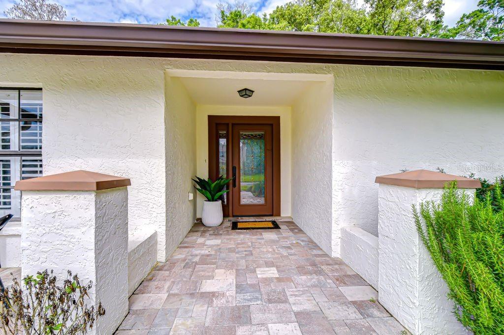 A covered entryway features a brown front door, a potted plant, and stone paver flooring — 16704 VALLELY DRIVE, TAMPA, FL