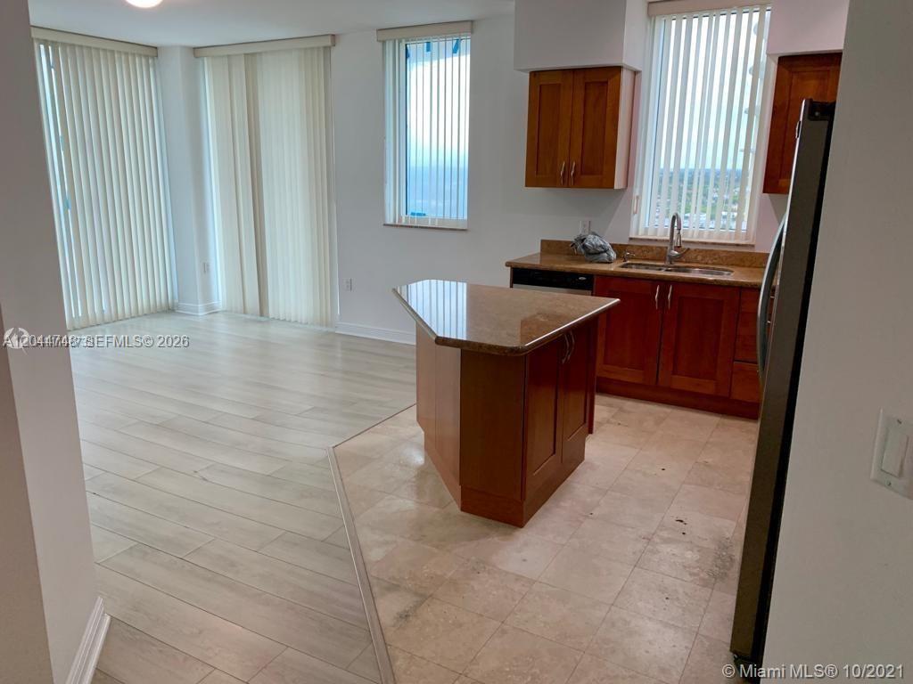 A kitchen with wood cabinets and a granite island sits next to a living area — 1755 E Hallandale Beach Blvd # 1907E, Hallandale Beach FL 33009, HALLANDALE BEACH, FL