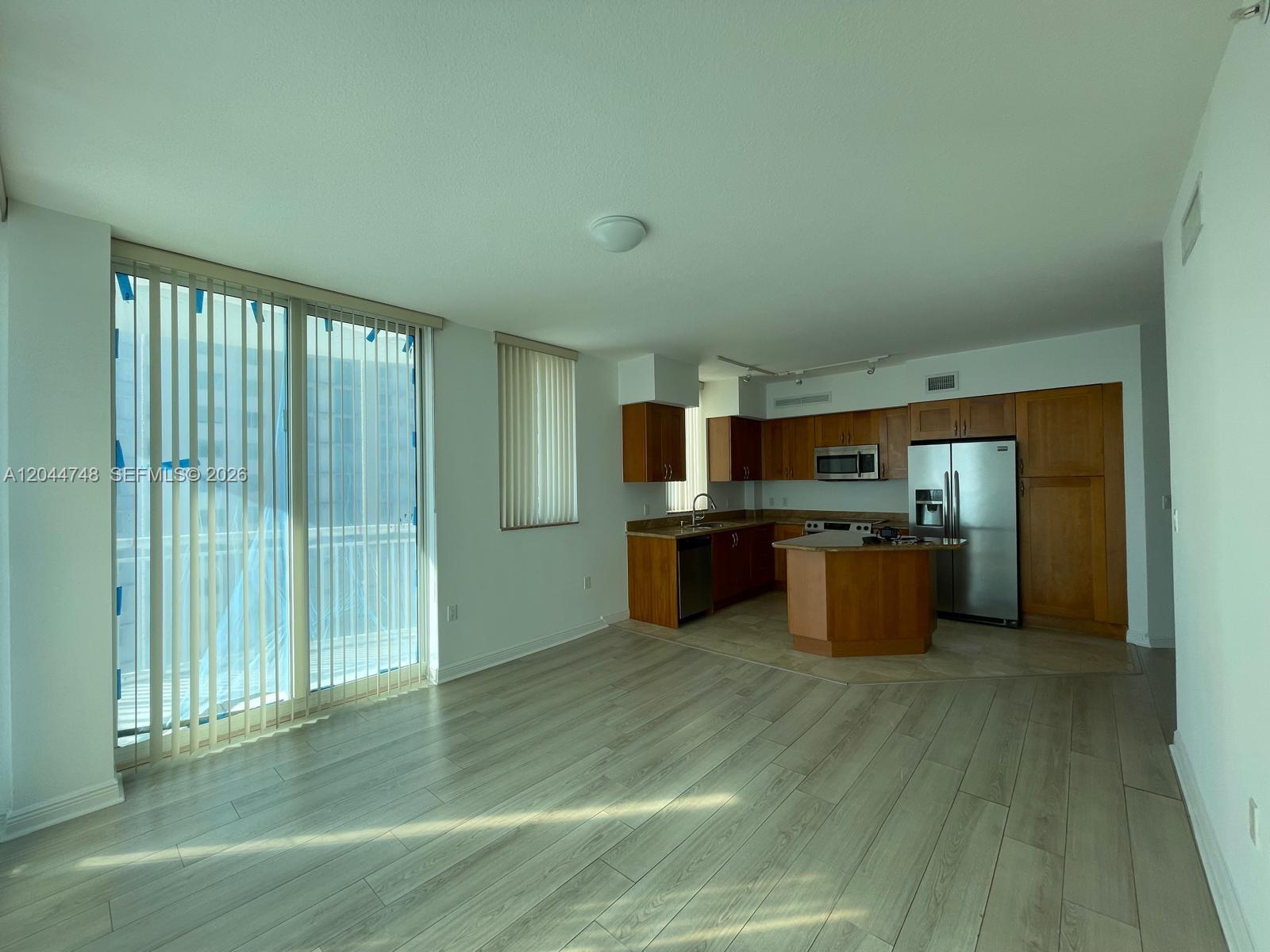 An open-concept living area features light wood-look flooring and a kitchen with wooden cabinets — 1755 E Hallandale Beach Blvd # 1907E, Hallandale Beach FL 33009, HALLANDALE BEACH, FL