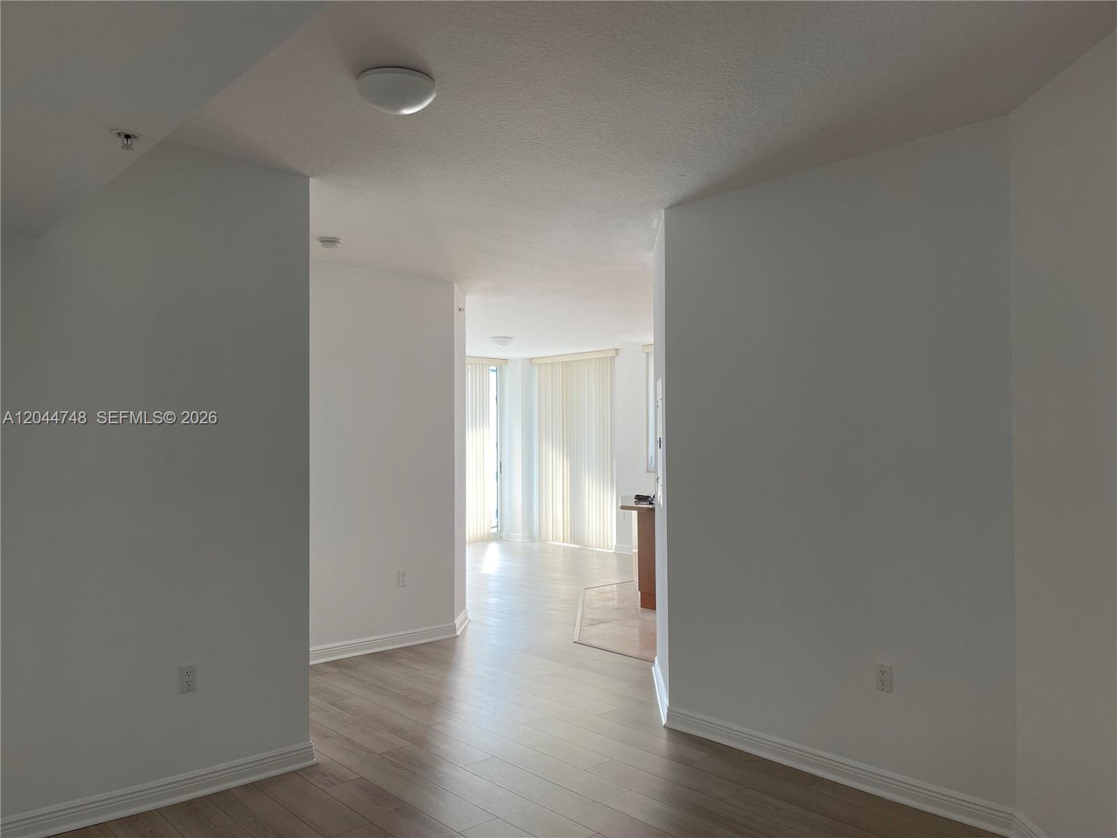 A view through a hallway into a bright living area with light wood flooring — 1755 E Hallandale Beach Blvd # 1907E, Hallandale Beach FL 33009, HALLANDALE BEACH, FL