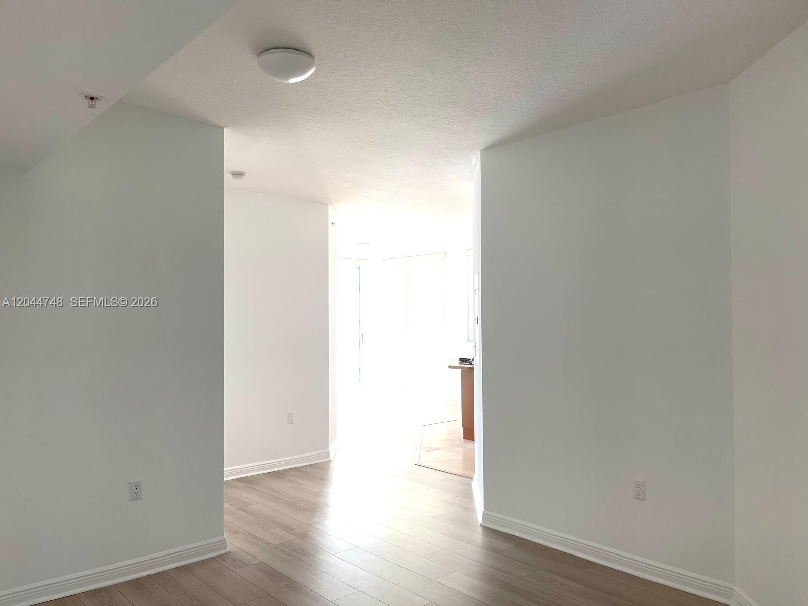 A bright hallway with light wood-look flooring connects two rooms in an empty apartment — 1755 E Hallandale Beach Blvd # 1907E, Hallandale Beach FL 33009, HALLANDALE BEACH, FL