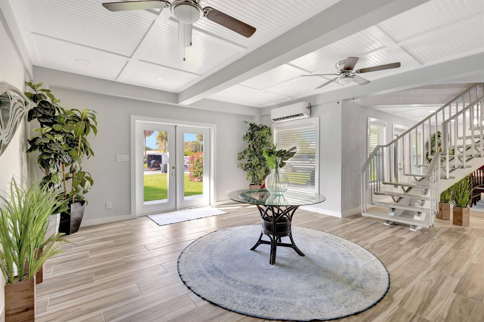 A bright entryway features a glass-topped table, a circular rug, and a staircase — 10355 Seagrape Way, Palm Beach Gardens FL 33418, PALM BEACH GARDENS, FL